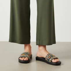 Person wearing black sandals with floral patterns and green pants on a neutral background