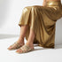 Person wearing gold gladiator flat sandals and a gold skirt on a white background