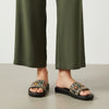 Person wearing black sandals with floral patterns and green pants on a neutral background
