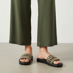 Person wearing black sandals with floral patterns and green pants on a neutral background