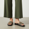Person wearing black sandals with floral patterns and green pants on a neutral background