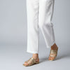 Gold gladiator sandals worn with white pants on a gray background