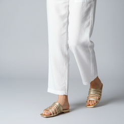 Gold gladiator sandals worn with white pants on a gray background