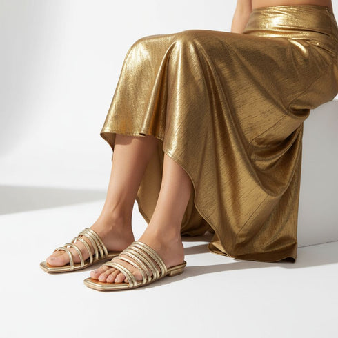 Person wearing gold gladiator flat sandals and a gold skirt on a white background